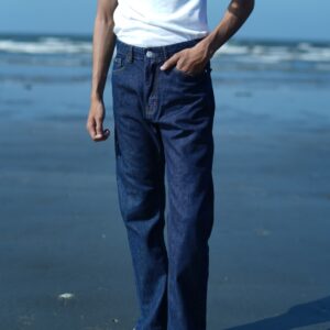 Men's dark blue straight fit denim jeans paired with a white t-shirt and white sneakers, photographed on a beach shoreline.